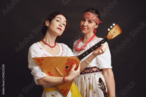 Women musicians in Russian folk dresses with musical instruments on a black studio background. Happy artists from Russia in white national clothes with stringed musical instruments