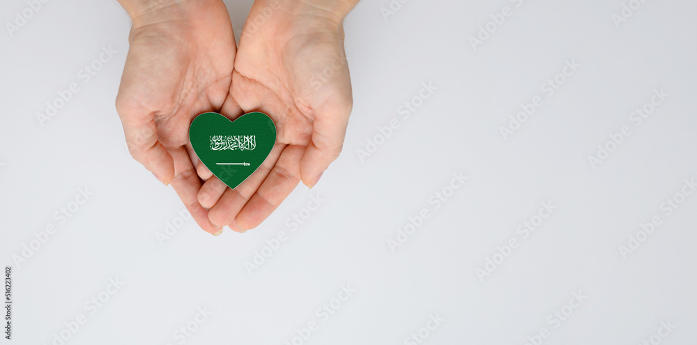 The national flag of Saudi Arabia in the shape of a heart of arms in female hands. Flat lay, copy space.