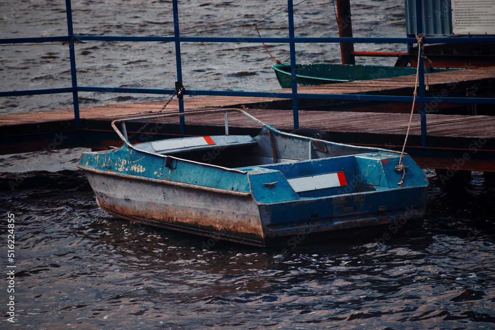 Rusty blue river boat moored to the pier. Cold windy weather and dark blue lake water. Abandoned place concept
