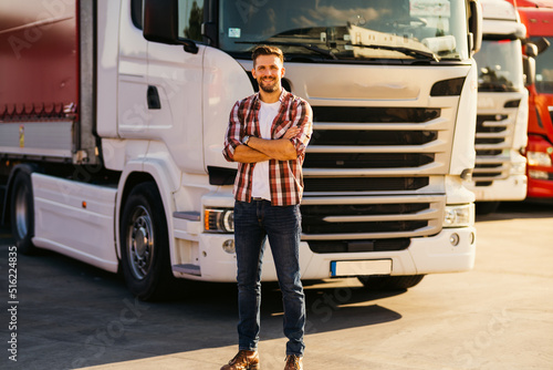 Portrait of young bearded man standing by his truck. Professional truck driver with crossed arms standing by semi truck vehicle. photo