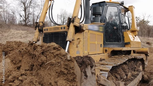 Bulldozer at construction site shovels soil into a heap. Powerful yellow earthmover crumbles sand at erection site. Bulldozer for paving the road, commercial vehicle.