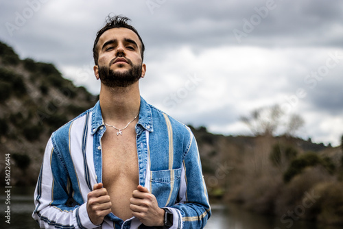 Canvas-taulu Portrait of a stylish young man opening his shirt with his head tilted back in nature