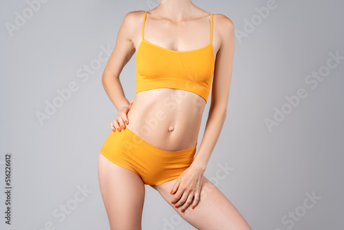 Slim woman in yellow underwear on gray background