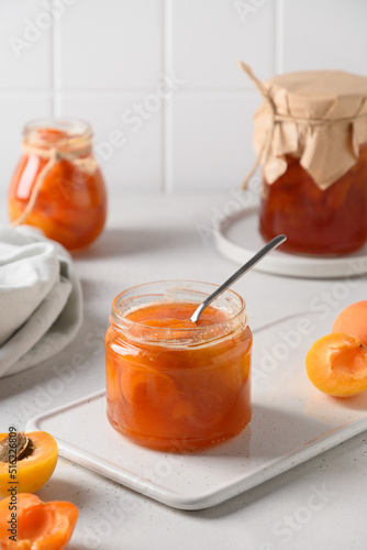 Apricot jam in glass jar with fruits on white background. Summer harvest and canned food. Tasty dessert. Close up.