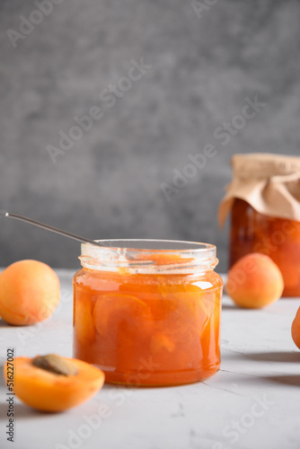 Apricot jam in glass jar for winter on gray background. Summer harvest and canned food. Tasty dessert. Vertical format. Close up.