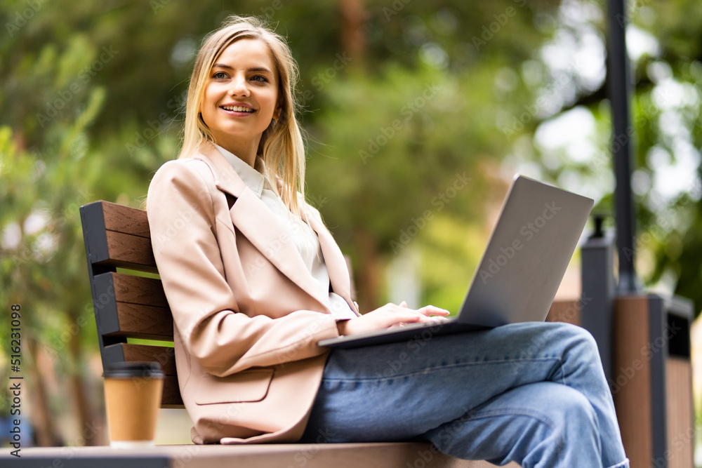 Young woman in eyeglasses sitting on bench in park and using laptop computer Young woman in eyeglasses sitting on bench in park and using laptop computer