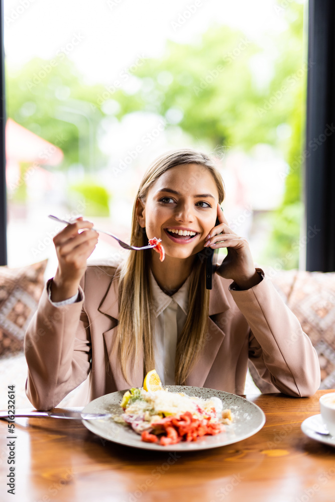 Pretty young woman eating salad in a cafe and talking on the phone