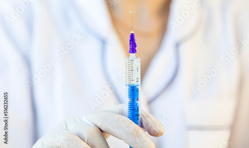 A female doctor holds a syringe in front of her, filled with medicine for injection. Focus on the syringe