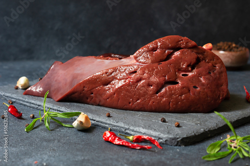 Fotografie Raw Beef liver meat on stone board with thyme and black peppers, cattle giblets