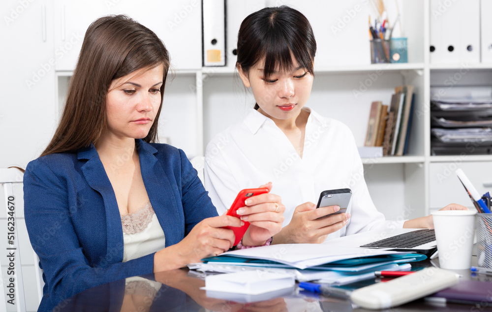 Obraz premium Two businesswomen working with smartphone in the office. High quality photo