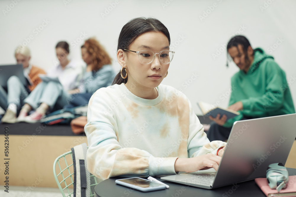 Serious teenage girl concentrating on schoolwork while sitting in front of laptop and looking for online information for new project Serious teenage girl concentrating on schoolwork while sitting in front of laptop and looking for online information for new project