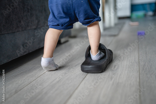 one caucasian toddler girl child playing with slippers at home in room alone putting on her feet walking copy space growing up and childhood development concept back view