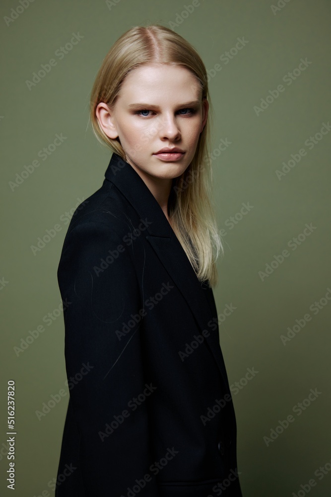 Fototapeta premium The young model turns and looks at the camera over her shoulder. Cool banner offer. A girl poses in isolation in a suit in a studio with a green background