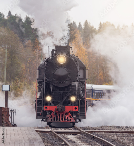 Retro steam train arrives to the station wooden platform. Ruskeala Mountain Park. Republic of Karelia.