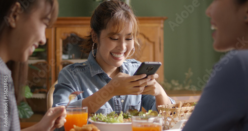 Asia young smart casual girl group friend sit at indoor coffee shop table enjoy laugh fun eat food drink lunch meal party at cafe. Relax look read e-mail text  money trade or post IG reel story app.