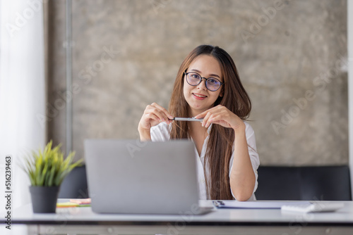 Image of young beautiful joyful asian businesswoman or asian student smiling in eyeglasses while working with laptop in home office