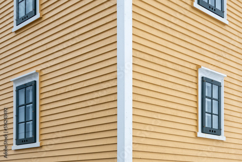 Wallpaper Mural A bright yellow wooden cape cod horizontal siding covered building in the background. The house has multi single double hung vintage windows in the exterior wall with green and white decorative trim.  Torontodigital.ca
