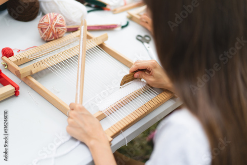 Girl weaving small rug with pattern at masterclass on weaving. Girl is studying how to weave on manual table loom. Process of creation. Handmade concept