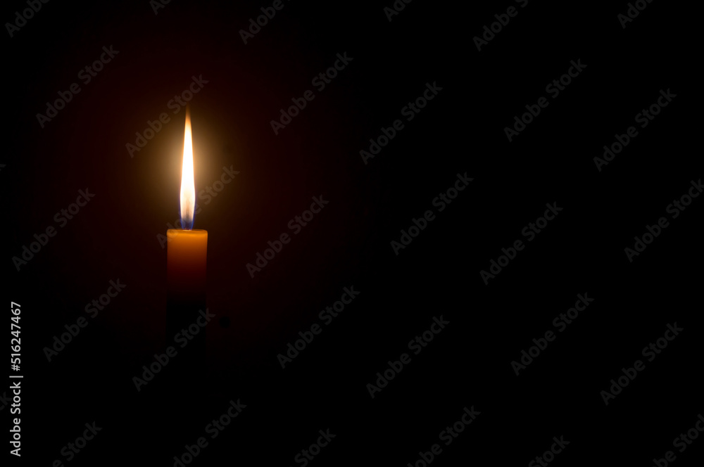 A single burning candle flame or light glowing on a Single small yellow candle is isolated on black or dark background on table in church or temple for Christmas, funeral or memorial service A single burning candle flame or light glowing on a Single small yellow candle is isolated on black or dark background on table in church or temple for Christmas, funeral or memorial service
