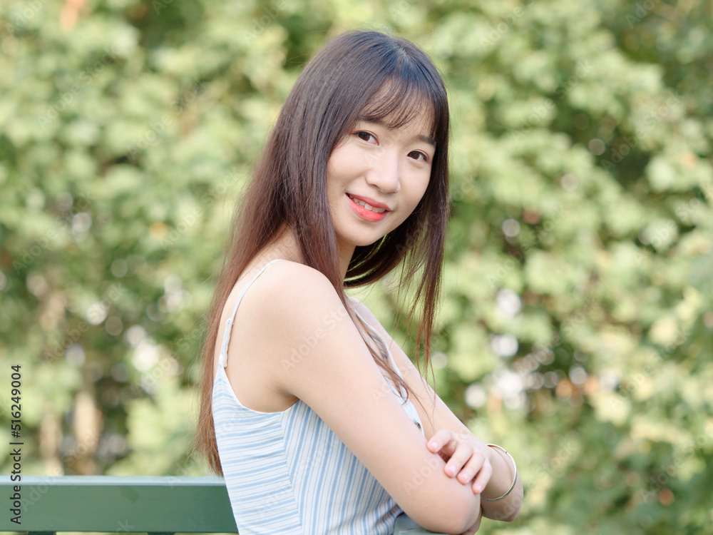 Portrait of beautiful Chinese girl with black long hair in sundress looking and smiling in park in sunny day. Outdoor fashion portrait of glamour young Chinese cheerful stylish woman. Portrait of beautiful Chinese girl with black long hair in sundress looking and smiling in park in sunny day. Outdoor fashion portrait of glamour young Chinese cheerful stylish woman.
