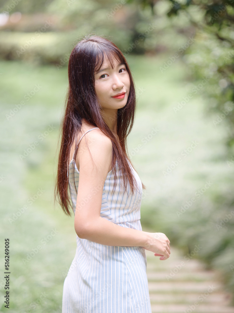 Portrait of beautiful Chinese girl with black long hair in sundress looking and smiling in park in sunny day. Outdoor fashion portrait of glamour young Chinese cheerful stylish woman. Portrait of beautiful Chinese girl with black long hair in sundress looking and smiling in park in sunny day. Outdoor fashion portrait of glamour young Chinese cheerful stylish woman.