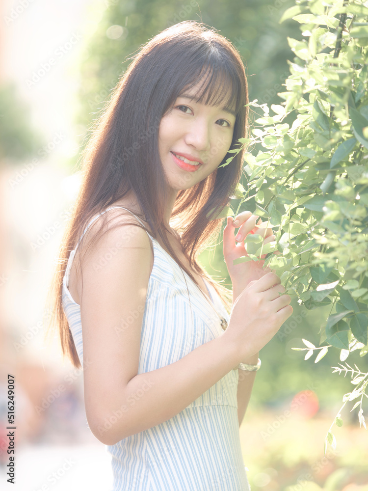 Portrait of beautiful Chinese girl with black long hair in sundress looking and smiling in park in sunny day. Outdoor fashion portrait of glamour young Chinese cheerful stylish woman. Portrait of beautiful Chinese girl with black long hair in sundress looking and smiling in park in sunny day. Outdoor fashion portrait of glamour young Chinese cheerful stylish woman.
