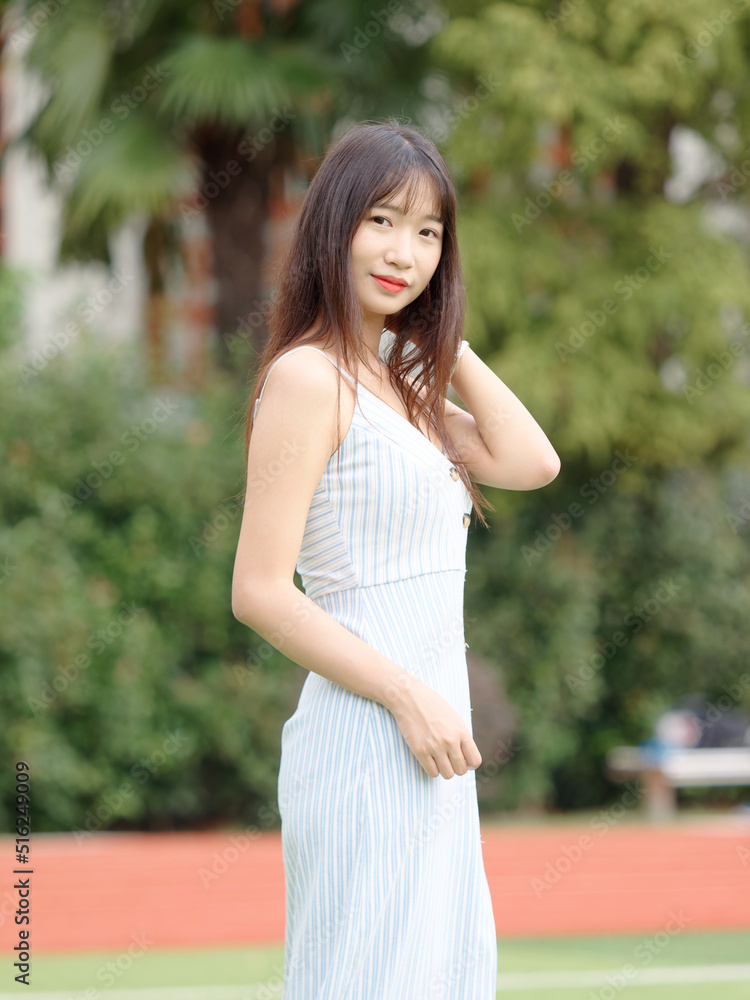 Portrait of beautiful Chinese girl with black long hair in sundress looking and smiling in park in sunny day. Outdoor fashion portrait of glamour young Chinese cheerful stylish woman. Portrait of beautiful Chinese girl with black long hair in sundress looking and smiling in park in sunny day. Outdoor fashion portrait of glamour young Chinese cheerful stylish woman.
