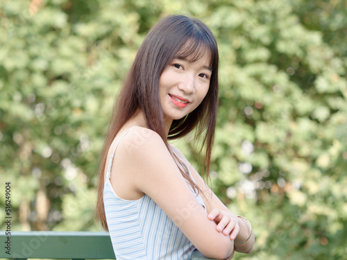 Portrait of beautiful Chinese girl with black long hair in sundress looking and smiling in park in sunny day. Outdoor fashion portrait of glamour young Chinese cheerful stylish woman.
