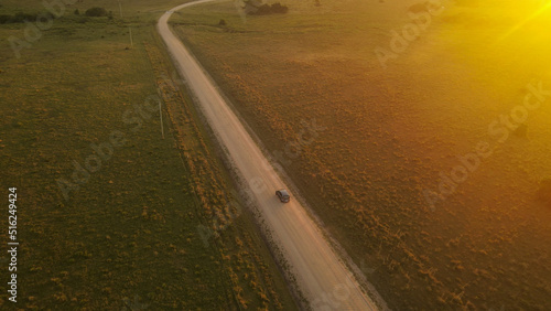 Cinematic shot of car driving on sandy road in middle of green growing national park at sunset