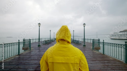 A lonely tourist in a yellow raincoat strolling at pier. Blonde woman enjoying astonishing urban panorama surrounded by stormy waterscape. High quality 4k footage