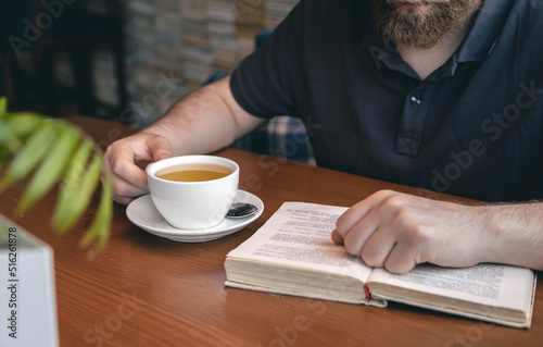 Close-up, a cup of tea and a book in male hands.