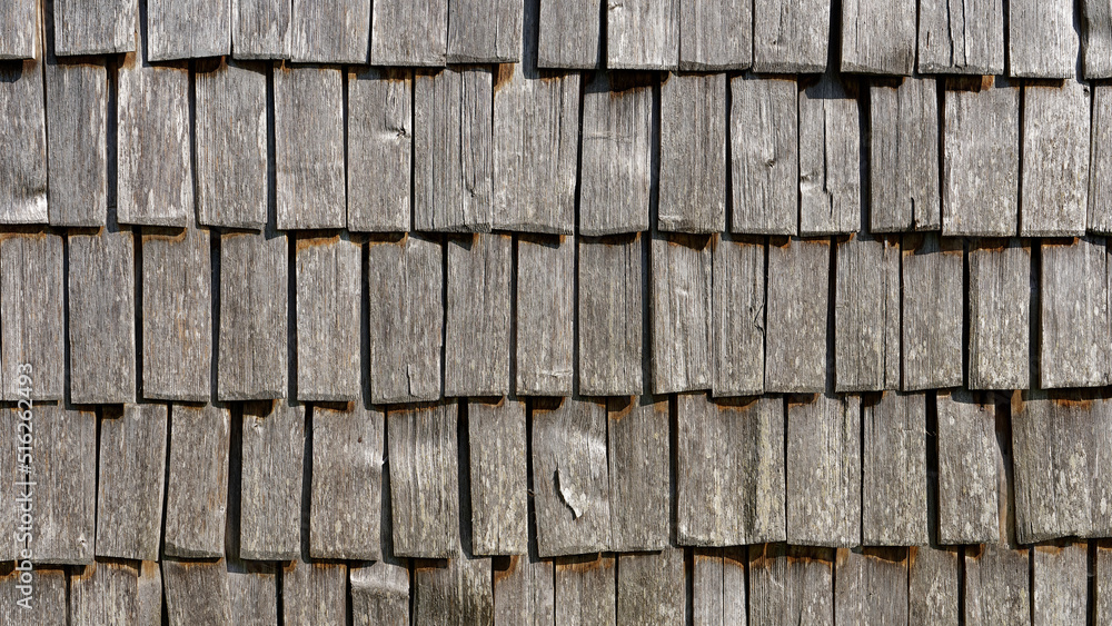 Strongly weathered, facade cladding of weathered wooden shingles on a field barn in the Alps. Copy space for your design. Web banner. Strongly weathered, facade cladding of weathered wooden shingles on a field barn in the Alps. Copy space for your design. Web banner.