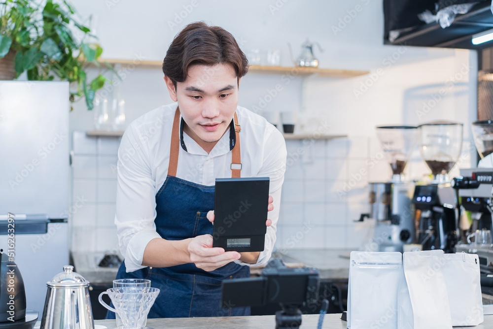 Asian businessman cafe owner record video of product for sale marketing. Handsome barista worker using camera livestreaming virtual or post advertising video for online digital social network content.