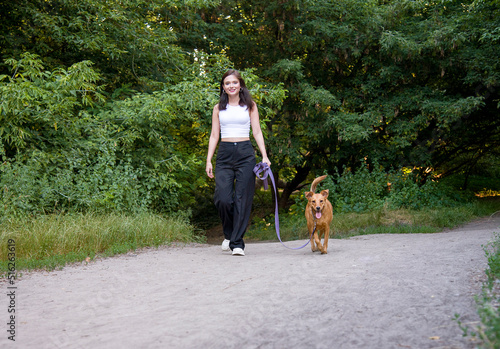 Young beautiful smiling woman walking with her dog in the woods
