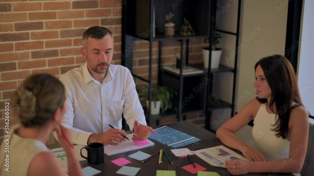 Three people are working and talking in the office. Papers with graphs and information Three people are working and talking in the office. Papers with graphs and information