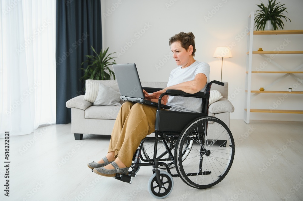 Middle age woman using laptop sitting on wheelchair at home Middle age woman using laptop sitting on wheelchair at home