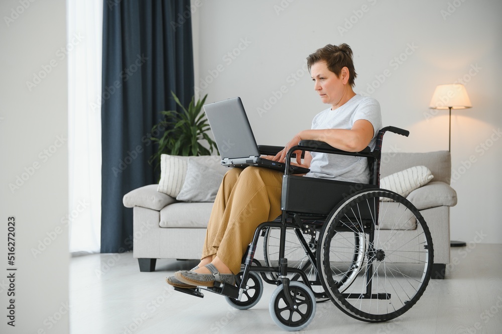 Middle age woman using laptop sitting on wheelchair at home Middle age woman using laptop sitting on wheelchair at home