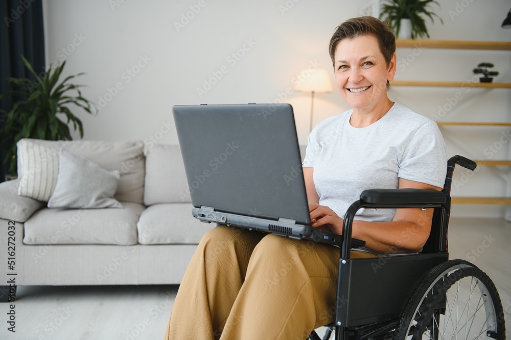 Positive elderly woman in wheelchair working on laptop, IT freelancer, online Positive elderly woman in wheelchair working on laptop, IT freelancer, online