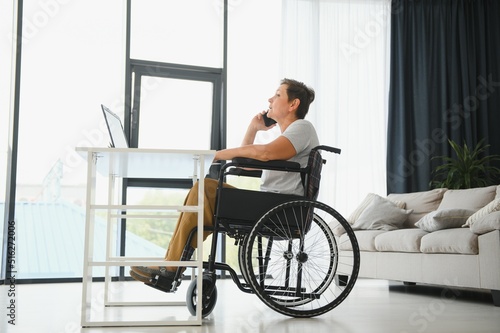 Middle age woman using laptop sitting on wheelchair at home
