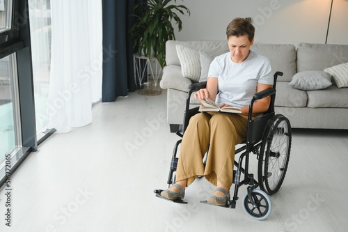 Shot of a senior woman sitting in a wheelchair and reading book at home