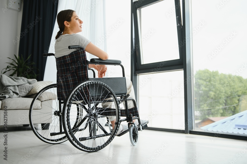 woman looking away while sitting in wheelchair at home