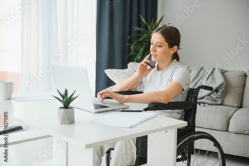 Female freelance programmer sitting in wheelchair and using computers while coding web game at home. © Serhii
