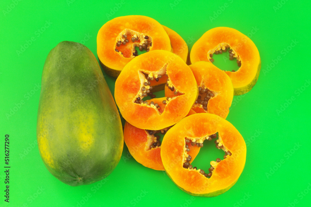 Papaya fruit slices and whole papaya fruit on green background.