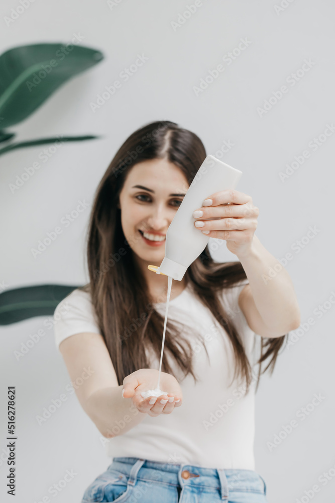 Happy woman pours shampoo in palm from plastic bottle in light studio Happy woman pours shampoo in palm from plastic bottle in light studio