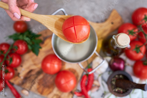 woman blanching a tomato holding over pan with hot water for further peeling