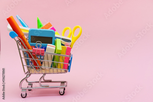 Blue shopping cart or trolley and stationery pen pencil clip pin rubber isolated on pink background. Online shopping concept for school