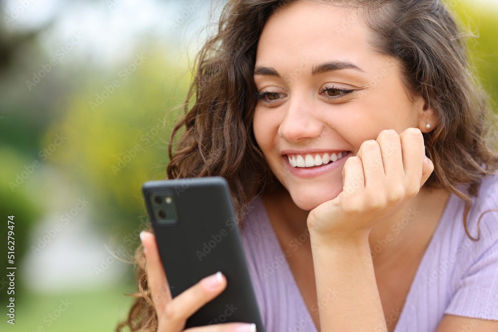 Happy woman checking smart phone in a park Happy woman checking smart phone in a park