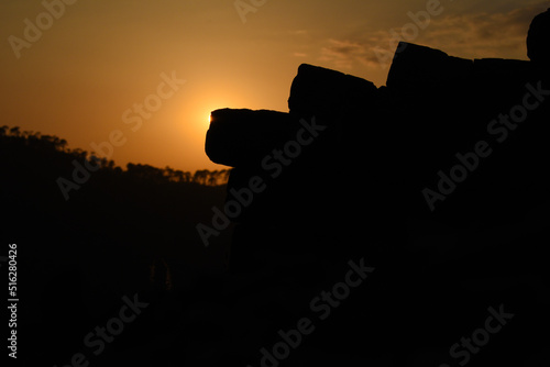 Silhouette photo of sun behind bricks, stones and trees on mountain in background