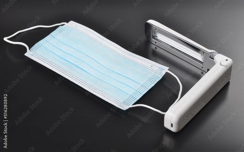 Portable quartz lamp with blue light disinfect medical mask on dark background from bacteria, virus, coronavirus, healthcare concept