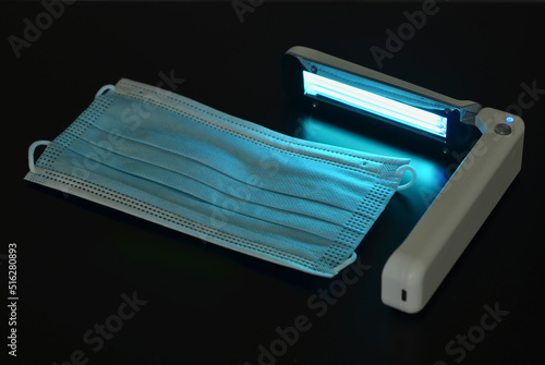 Portable quartz lamp with blue light disinfect medical mask on dark background from bacteria, virus, coronavirus, healthcare concept